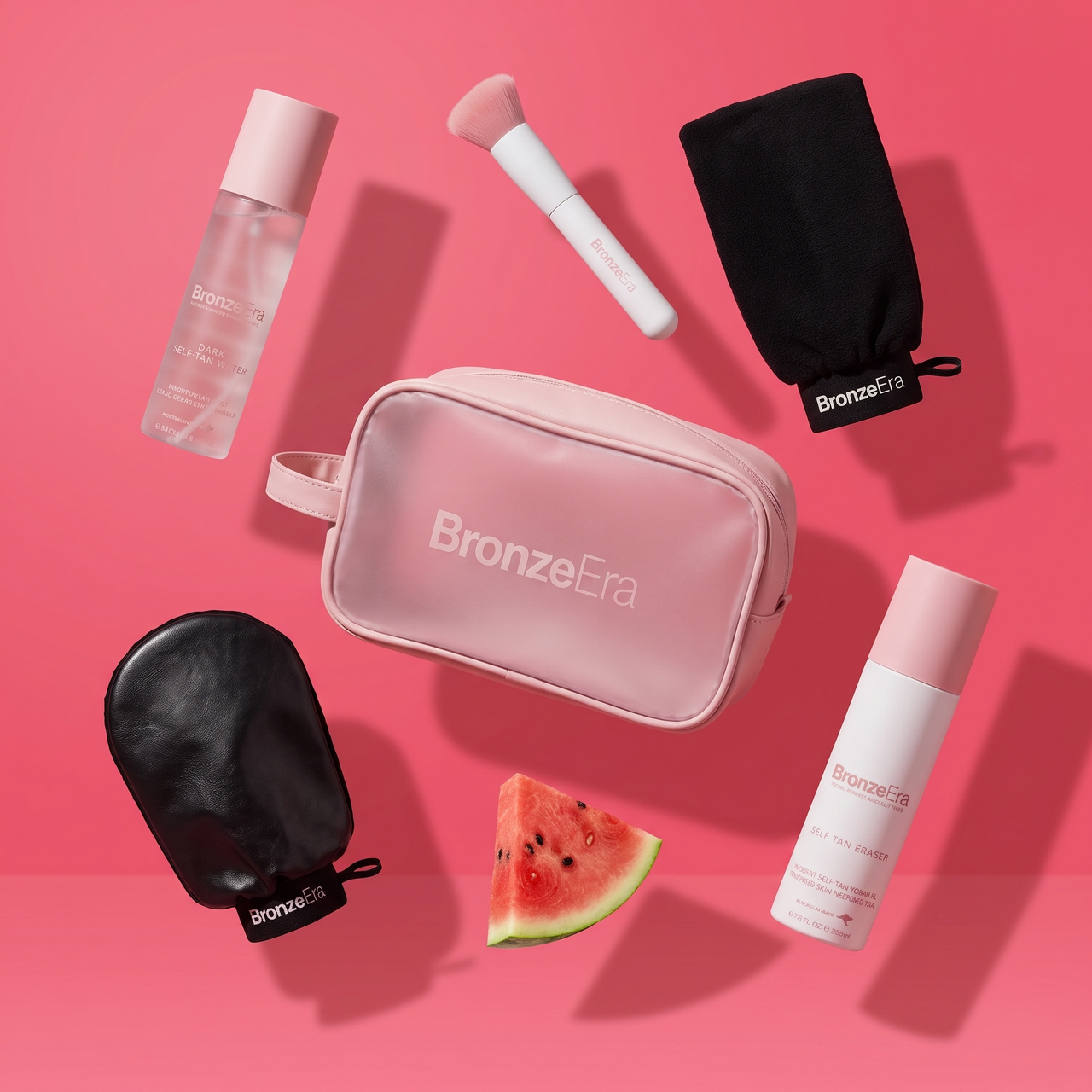 BronzeEra tanning kit flat lay on pink - travel bag, tanning mitts, brush, Dark Self-Tan Water and Self Tan Eraser